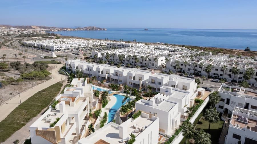 Aerial view of a whitewashed Spanish urbanization with pool and sea view